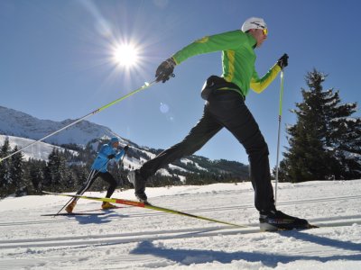 Zwei Langläufer fahren durch den Schnee, während die Sonne hell am Himmel scheint.