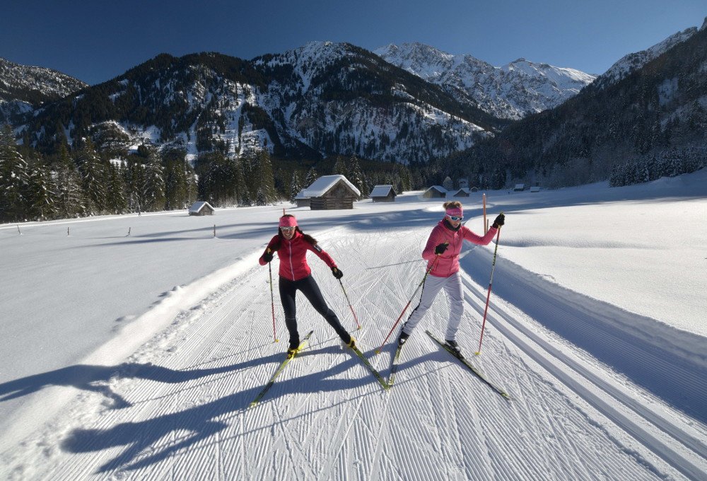 Zwei Langläuferinnen in rosa Jacken auf verschneiter Strecke.