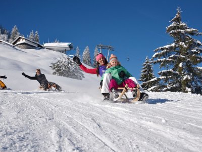 Familie beim Rodeln im Schnee auf einer verschneiten Bergwiese.