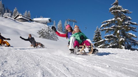 Familie beim Rodeln im Schnee auf einer verschneiten Bergwiese.
