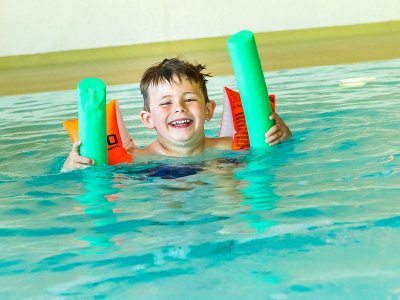 Lächelndes Kind mit Schwimmflügeln und Schwimmnudeln im Wasser.