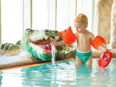 Kleines Kind mit Schwimmflügeln spielt mit einem Wasserspielzeug-Krokodil.