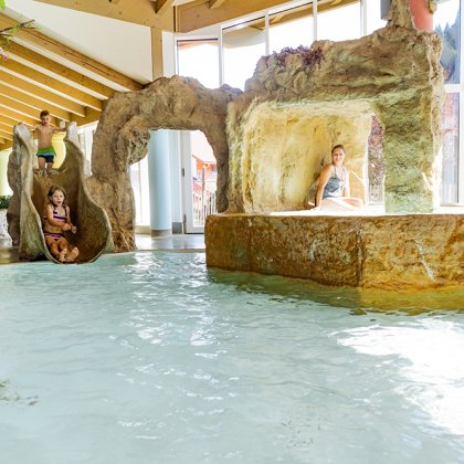 Kinder rutschen ins Hallenbad mit Felsenlandschaft und Grotte.