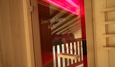 Eingang zur Zirben-Textilsauna mit rotem Licht und Glastür.