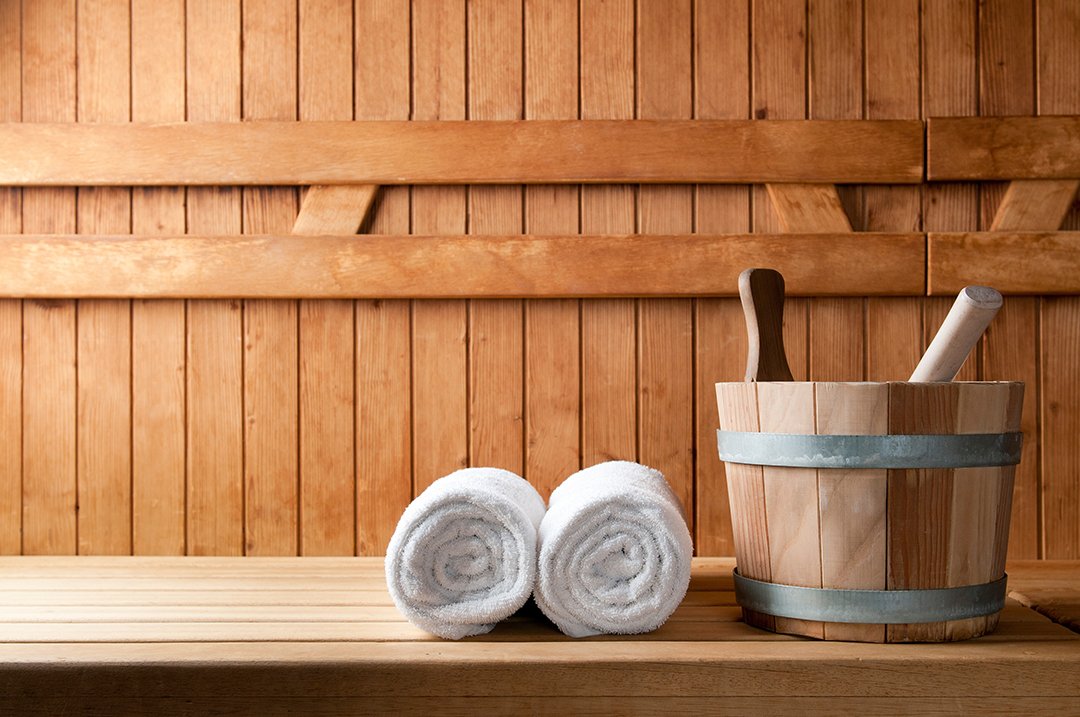 Weißer Handtuchstapel und ein Holzfass mit Holzstampfer in einer Sauna.