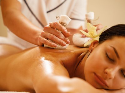 Frau erhält eine Massage mit Kräuterbeuteln in einem Wellnessbereich.