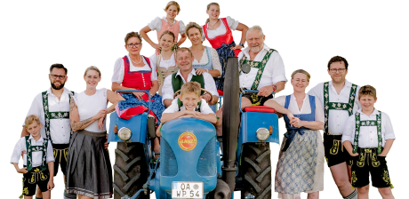 Eine Gruppe von Menschen in traditioneller bayerischer Tracht vor einem Traktor.