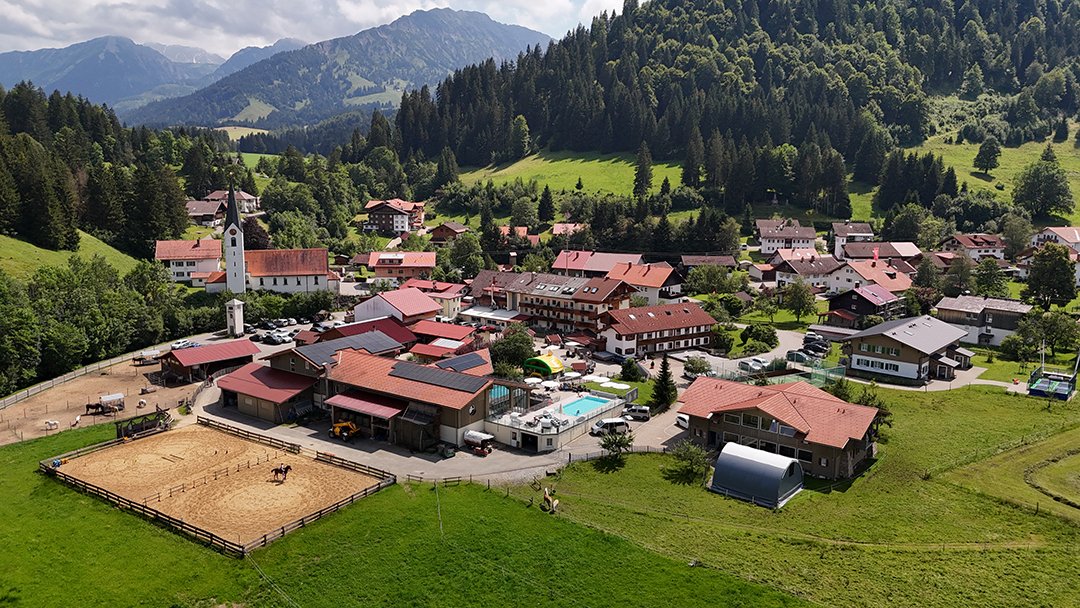 Das Bild zeigt ein malerisches Dorf mit rot gedeckten Häusern, einem Reitplatz und einem Poolbereich.