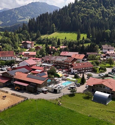 Das Bild zeigt ein malerisches Dorf mit rot gedeckten Häusern, einem Reitplatz und einem Poolbereich.