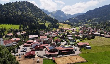Das Bild zeigt ein malerisches Dorf, umgeben von Bergen, mit einer Reitfläche und Häusern.