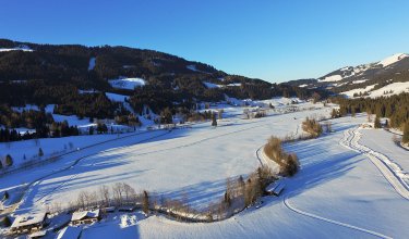 Das Bild zeigt eine verschneite Landschaft mit hügeligem Gelände und vereinzelten Häusern.