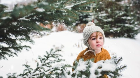 Ein kleines Kind in einem gelben Pullover und einer grauen Mütze steht im Schnee.