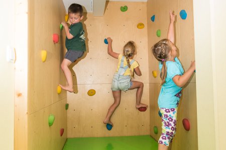 Drei Kinder klettern an einer Kletterwand in einem Spielraum.