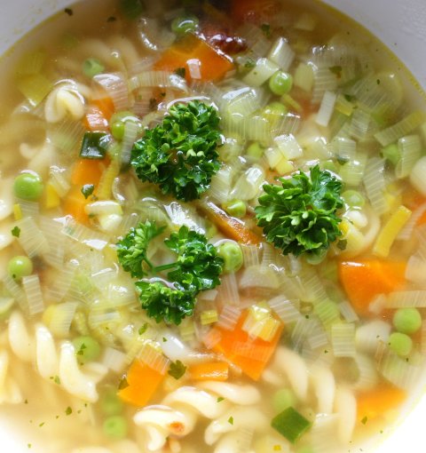 Teller mit Nudelsuppe und Gemüseeinlage.