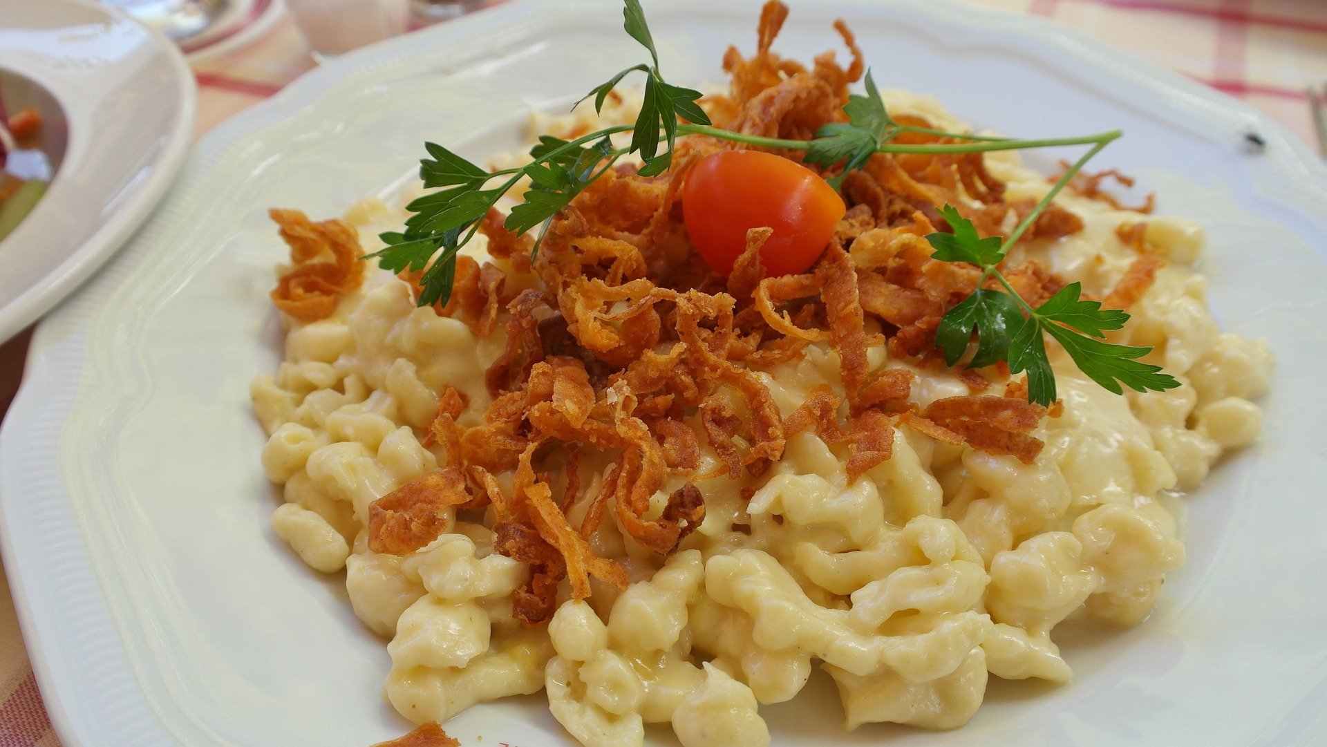 Käsespätzle mit Zwiebeln und einer Tomate auf Teller angerichtet.