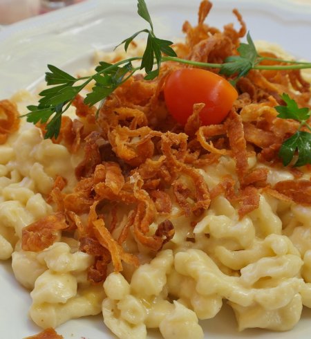 Käsespätzle mit Zwiebeln und einer Tomate auf Teller angerichtet.