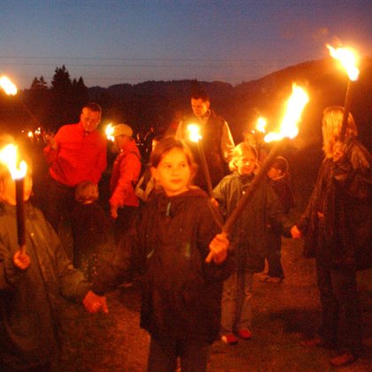 Kinder und Erwachsene gehen bei Nacht mit Fackeln auf einem Wanderweg.