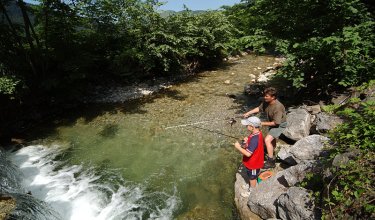 Vater und Sohn fischen zusammen an einem klaren Bachufer.
