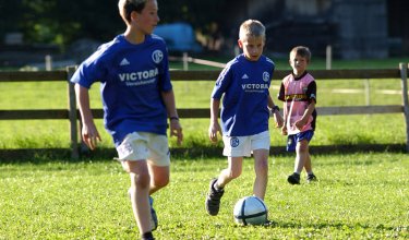 Kinder spielen Fußball auf einer Wiese.