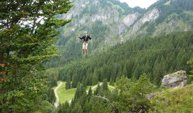 Eine Person balanciert auf einem Seil über dem Wald.
