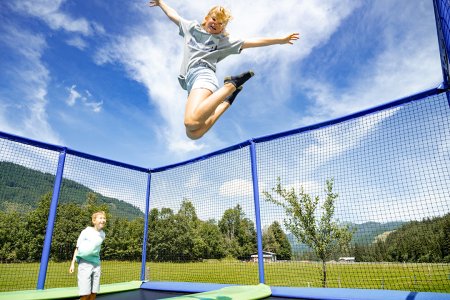 Kind springt hoch mit ausgebreiteten Armen auf Trampolin.