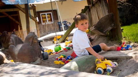 Ein Junge spielt mit Spielzeugen im Sandkasten auf einem Spielplatz.