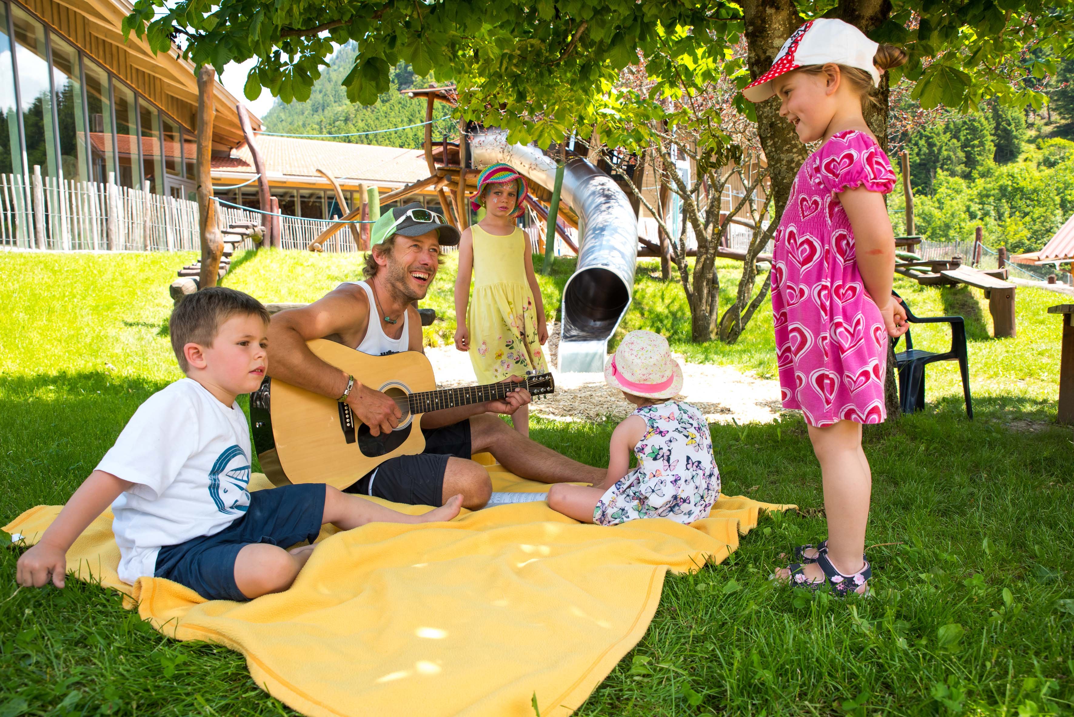 Ein Mann spielt Gitarre für Kinder im Freien.