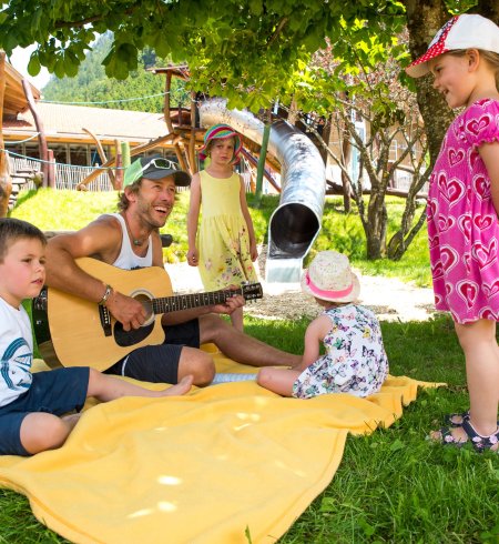 Ein Mann spielt Gitarre für Kinder im Freien.