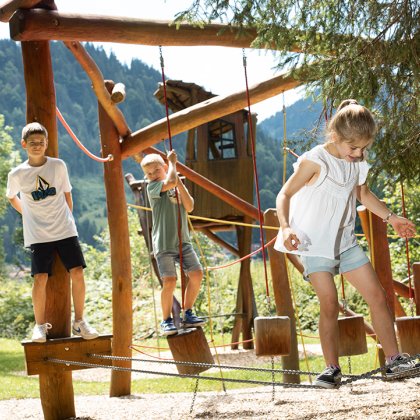 Kinder balancieren auf Seilen am Abenteuerspielplatz aus Holz.