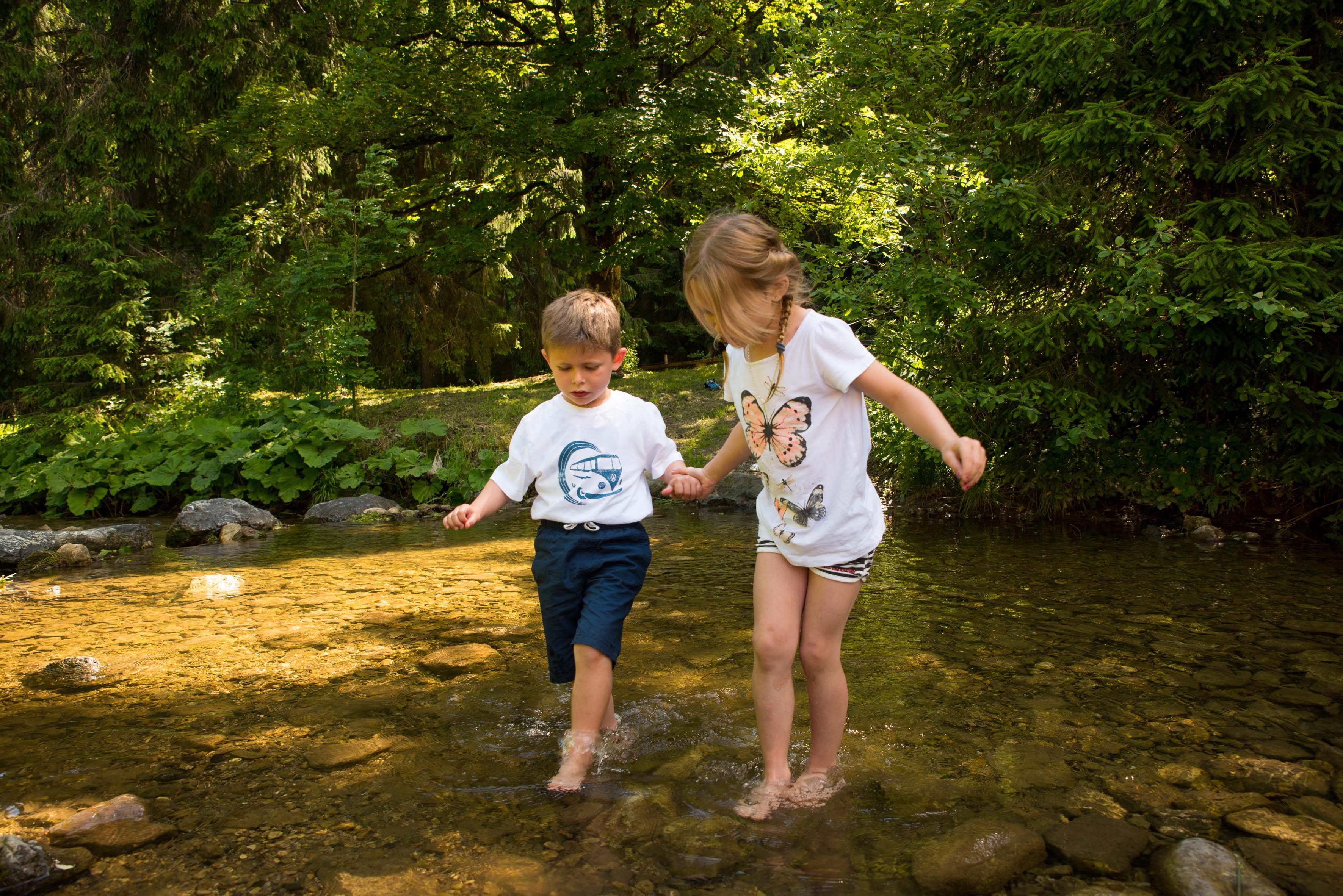 Kinder, die im Wasser stehen und miteinander Händchen halten.