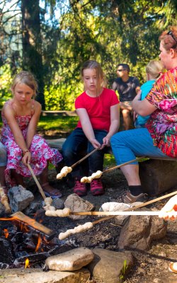 Kinder rösten Stockbrot über einem Lagerfeuer, während Erwachsene zuschauen.