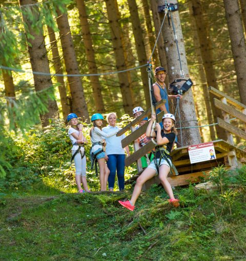 Eine Gruppe von Kindern fährt auf einer Seilrutsche im Wald.