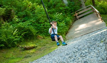 Ein Junge schwingt an einer Seilbahn im Wald.