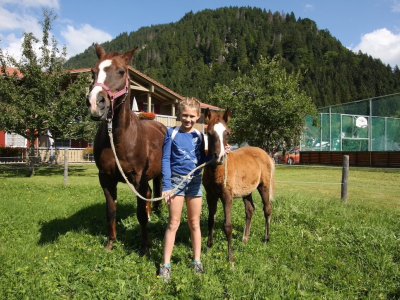 Ein Mädchen steht zwischen einem Pferd und einem Fohlen.