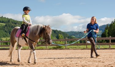 Ein Kind reitet ein Pony, während eine Betreuerin das Pony führt.