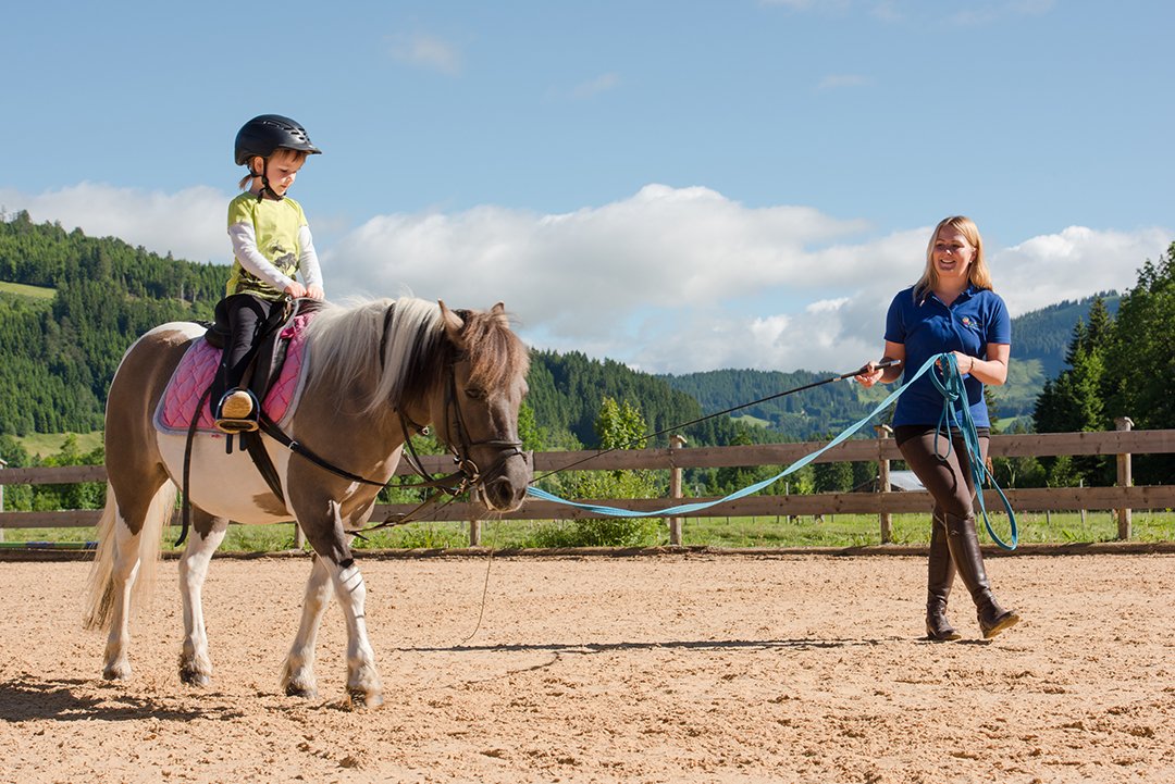 Ein Kind reitet ein Pony, während eine Betreuerin das Pony führt.