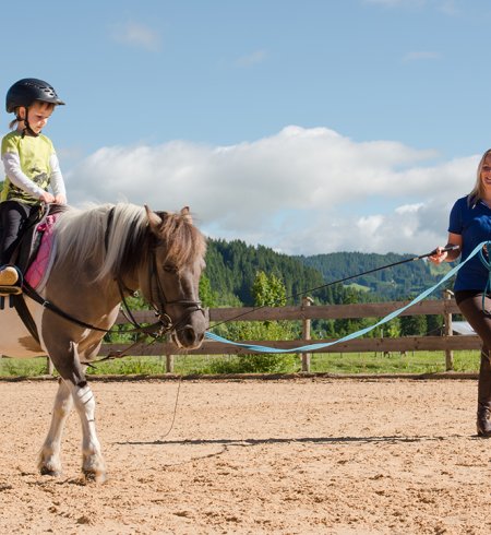 Ein Kind reitet ein Pony, während eine Betreuerin das Pony führt.