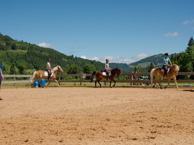 Reiterinnen reiten in einer Reitbahn, während eine Instruktorin auf dem Boden steht.