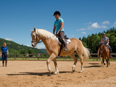 Eine Reiterin reitet auf einem Pferd in einem Reitstall, während die Instruktorin daneben geht.