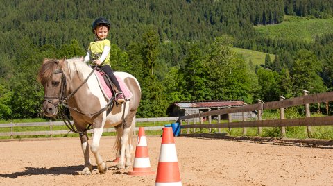 Ein Kind reitet auf einem Pony und passiert einen Parcours mit Kegeln.