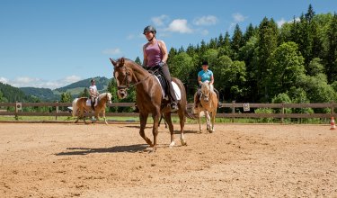 Reiterin reitet auf einem Pferd in der Reitbahn, während andere Reiterinnen hinter ihr reiten.