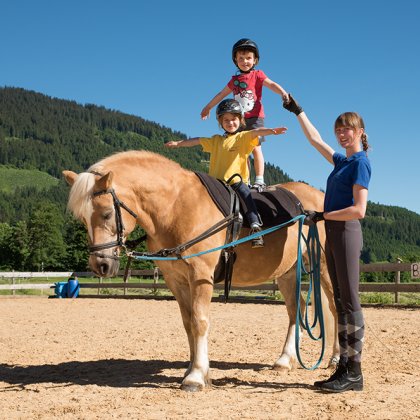 Zwei Kinder stehen auf einem Pony, das von einer Betreuerin gehalten wird.