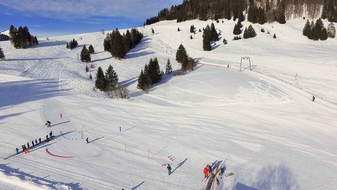 Ein verschneites Bergland mit Skifahrern auf den Pisten, der Skilift ist im Hintergrund sichtbar.