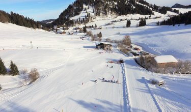 Ein verschneites Bergland mit Skifahrern auf den Pisten, der Skilift ist im Hintergrund sichtbar.