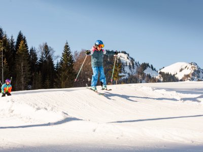 Mädchen auf Skiern springt über eine kleine Welle auf der Piste.