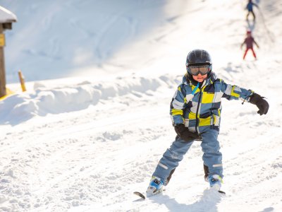Junge in buntem Skianzug fährt die Skipiste hinab.
