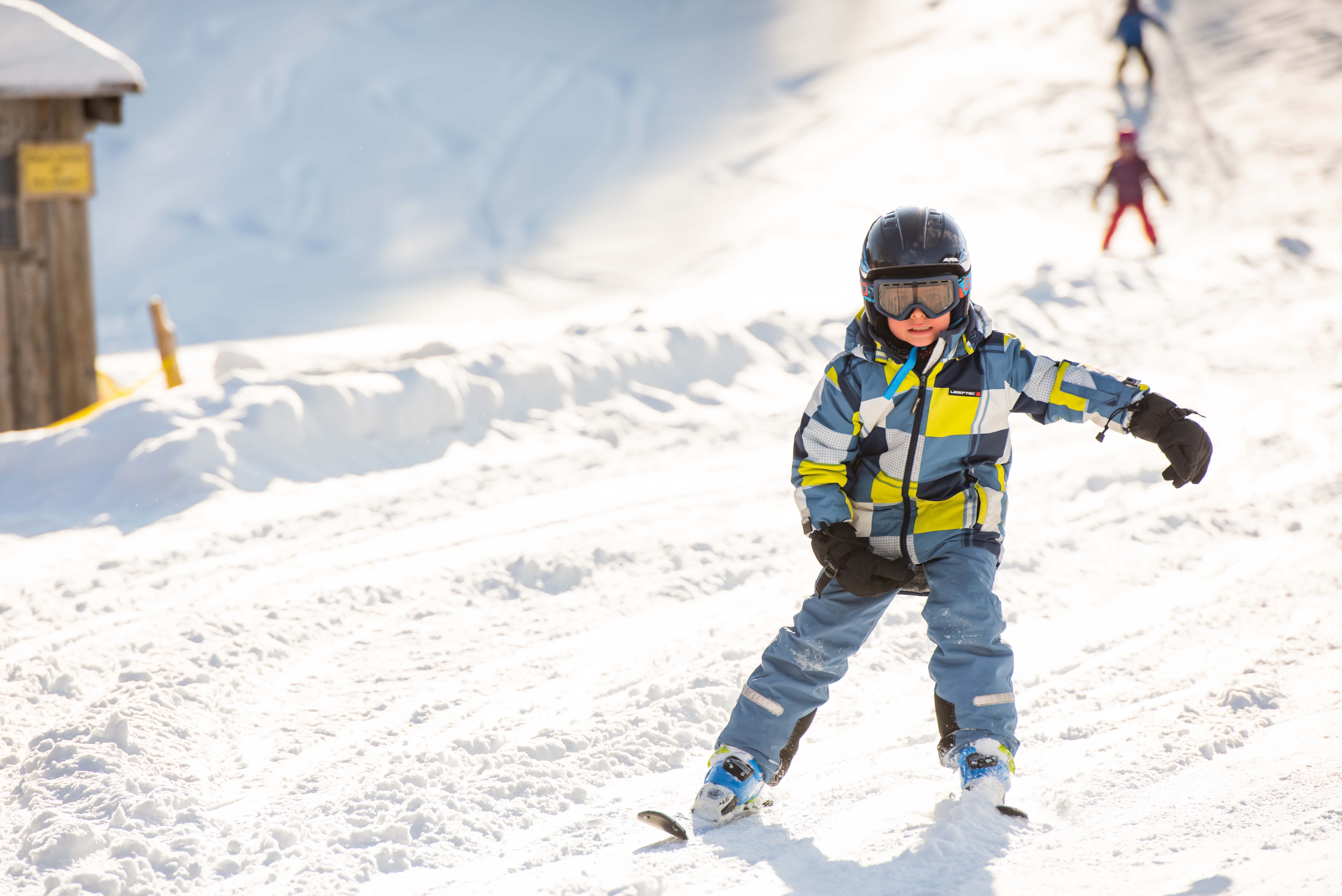 Junge in buntem Skianzug fährt die Skipiste hinab.