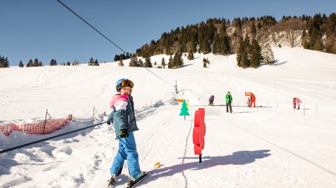 Mädchen fährt auf dem Kinderskilift die Piste bergauf.