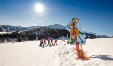 Skilehrer mit einer Gruppe Kinder beim Skikurs auf der verschneiten Piste.