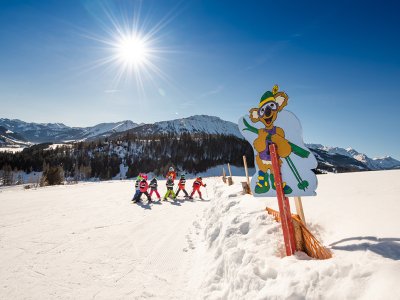 Skilehrer mit einer Gruppe Kinder beim Skikurs auf der verschneiten Piste.